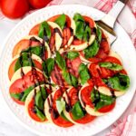 A round white plate filled with vegan Caprese salad with basil and balsamic glaze.