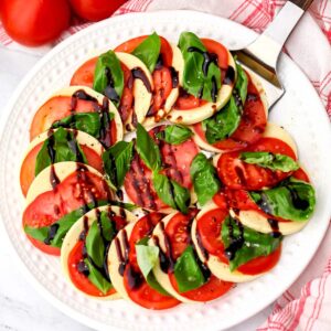 A round white plate filled with vegan Caprese salad with basil and balsamic glaze.