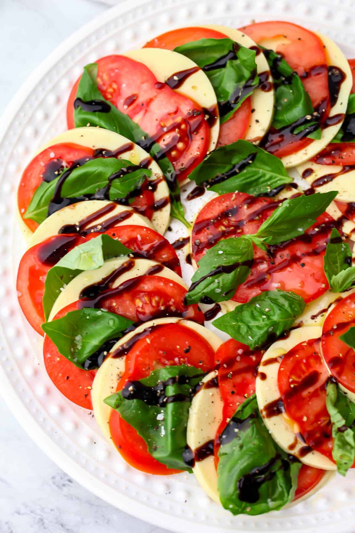A top view of a vegan Caprese salad with tomatoes, basil, and balsamic glaze.