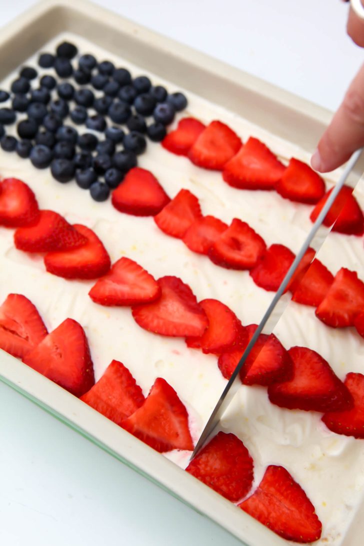 Cutting a vegan ice cream cake with berries on top in the shape of a flag.