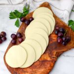 Vegan mozzarella slices on a cutting board with grapes around it.