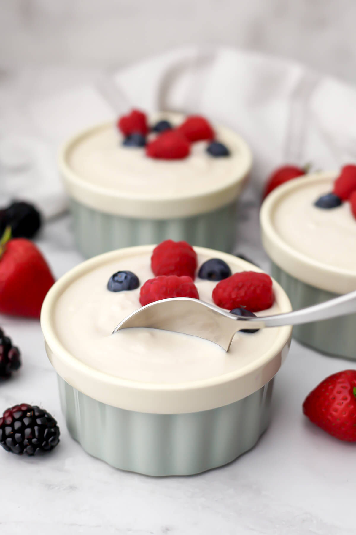 Vegan Greek yogurt in a small bowl with berries on top and a spoon scooping some out of the bowl.