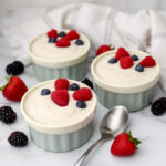 Three small cups filled with vegan Greek yogurt with berries on top and a spoon on the side.