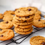 Vegan peanut butter chocolate chip cookies on a cooling wrack with a tea towel behind them.