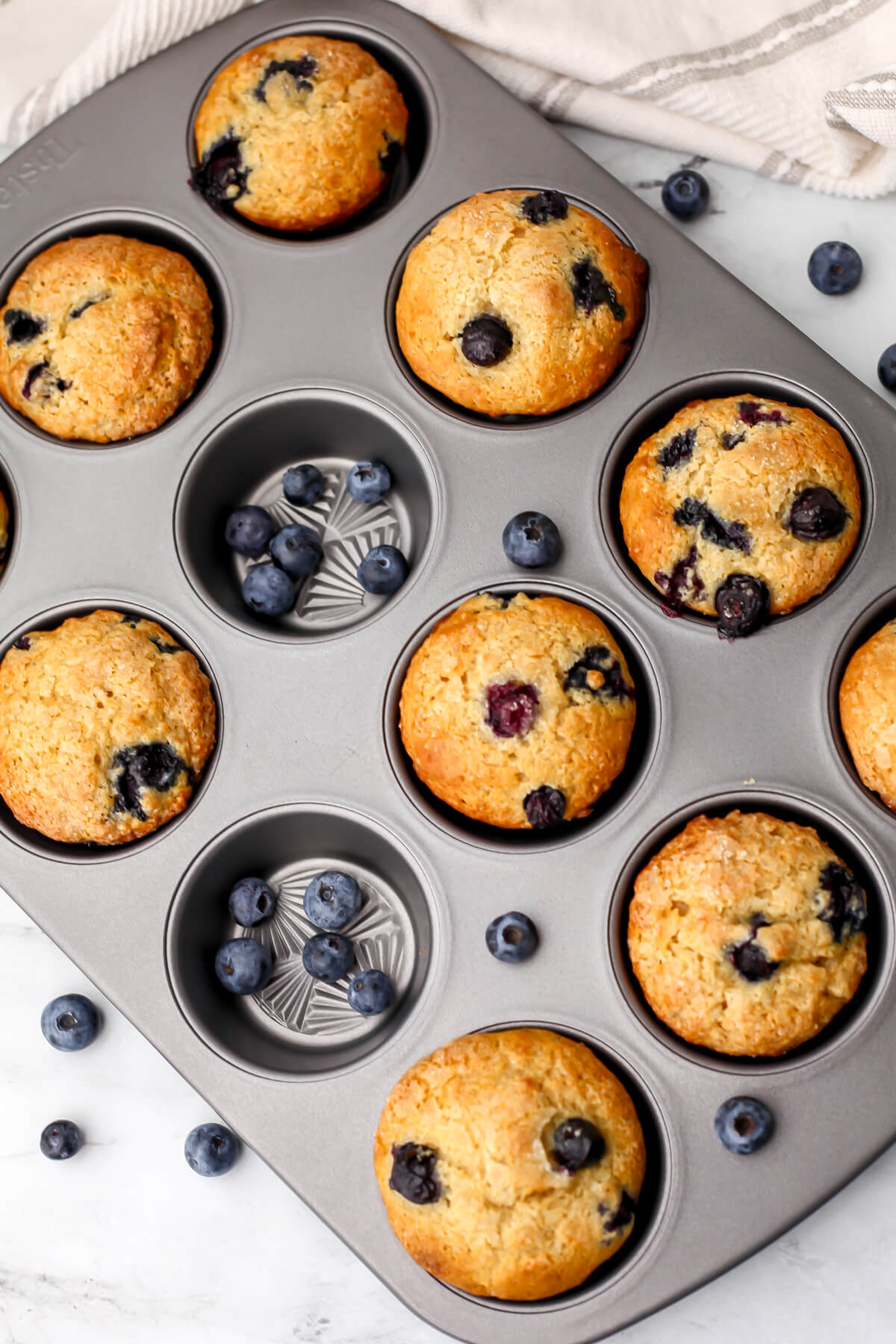 A top view of vegan blueberry protein muffins in a muffin tin with fresh blueberries around it.