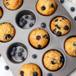 A top view of a muffin tin filled with vegan blueberry protein muffins with blueberries around it.