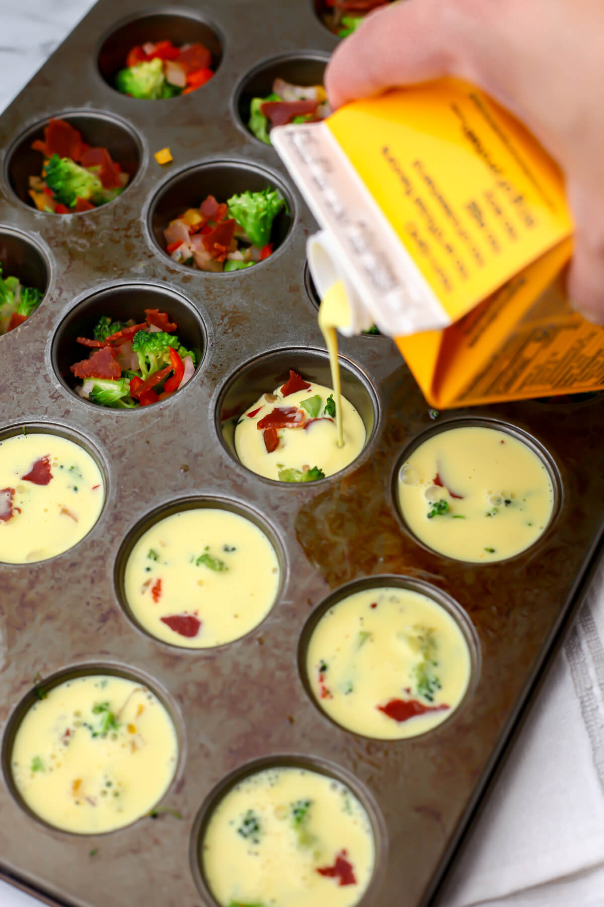 Just Egg being poured over sauteed veggies in a mini muffin tin to make vegan egg bites.