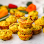 Vegan egg bites made from just egg on a marble counter top with vegetables behind them.