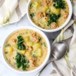 A top view of 2 bowls of vegan sausage and potato soup with kale with a spoon on the side.