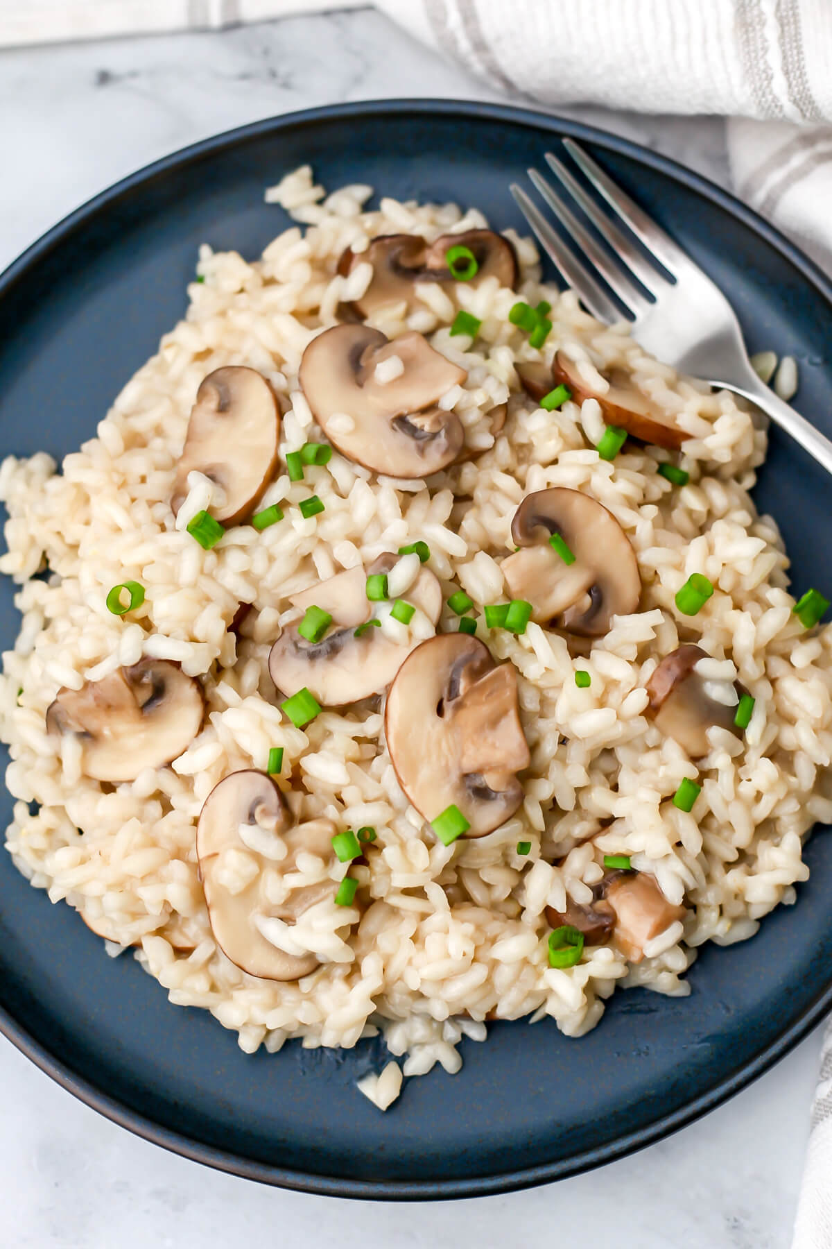 A top view of a plate of mushroom risotto with green onions sprinkled on top and a fork on the side.