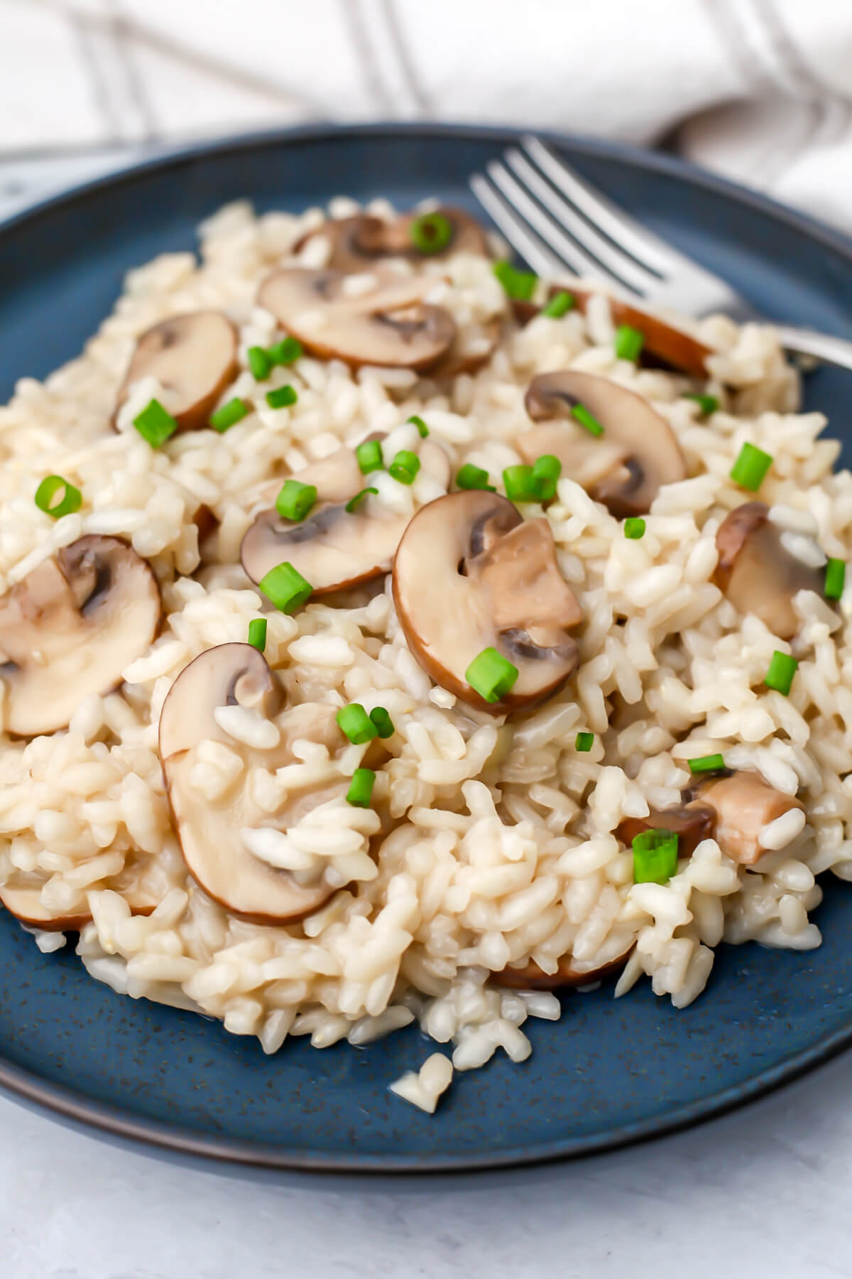 A blue plate filled with creamy vegan mushroom risotto with a fork on the side.