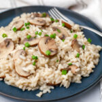 A blue plate filled with vegan mushroom risotto topped with green onions.