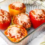 Quinoa stuffed pepper made with veggies, vegan sausage and quinoa topped with vegan cheese in a baking dish.
