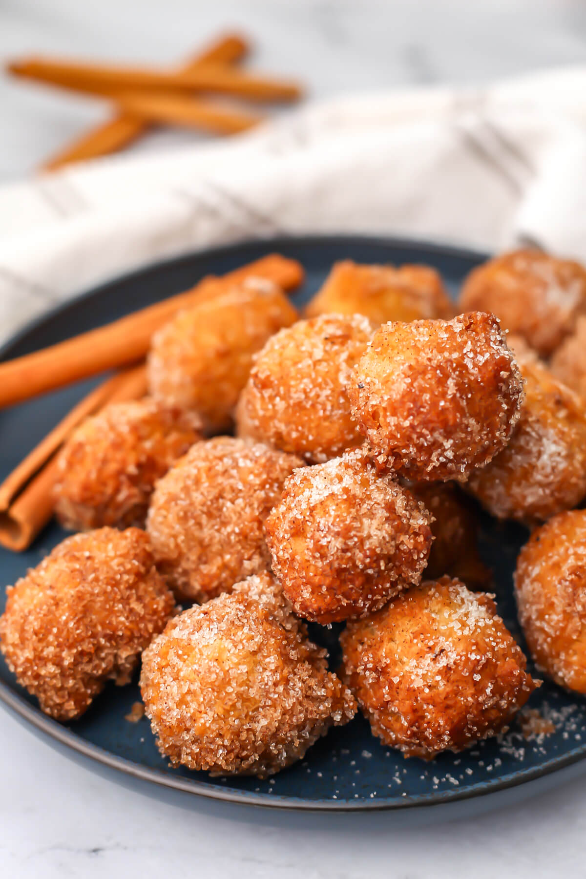 Vegan cinnamon and sugar donut holes on a blue plate with cinnamon sticks in the background.