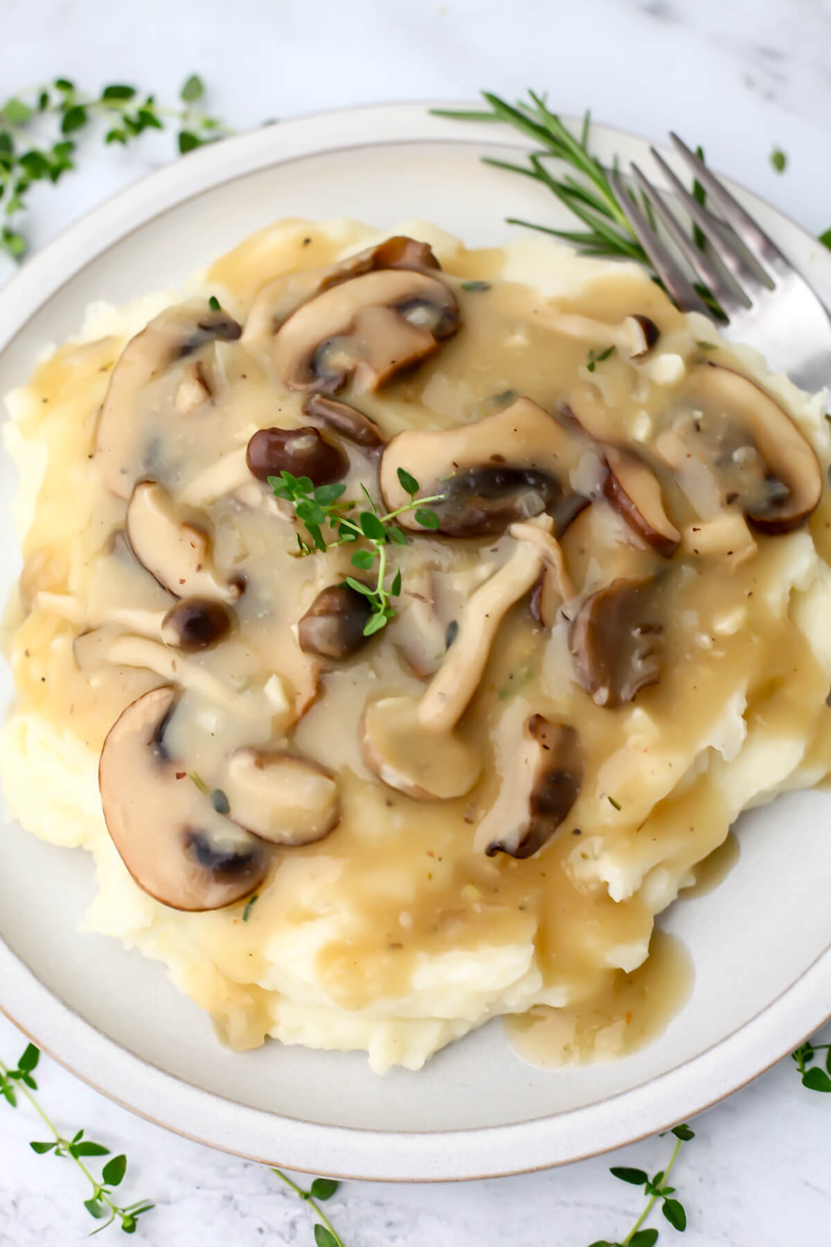 Vegan mushroom gravy served over mashed potatoes on a white plate with fresh herbs around.