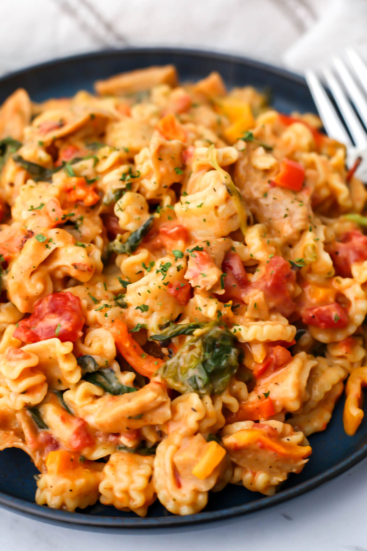 A blue plate filled with creamy vegan Cajun pasta with a fork on the side.