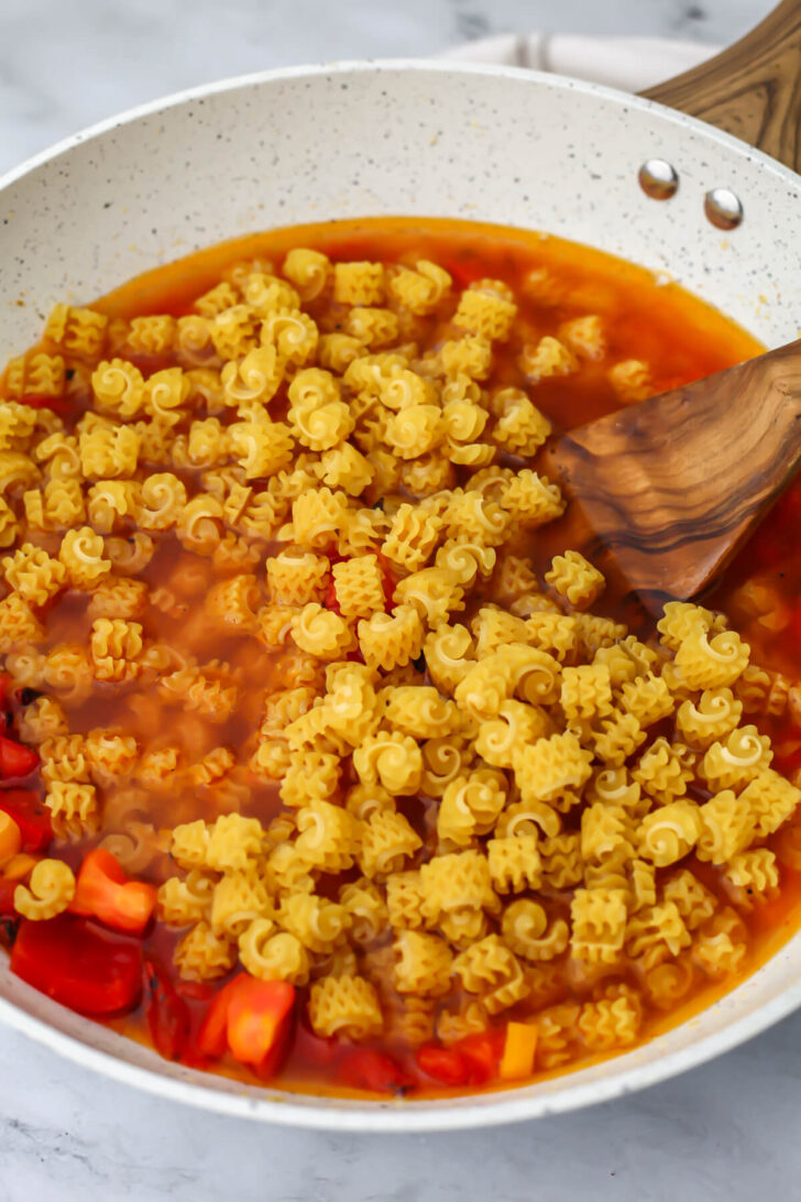 Pasta being added to broth and veggies to make Cajun pasta.