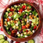 A top view of a vegan Greek salad in a wooden bowl.