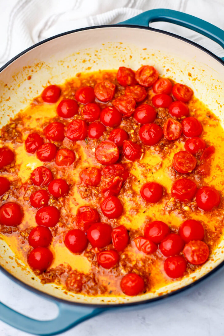 Garlic, ginger, cumin, and curry simmering in oil with cherry tomatoes added.