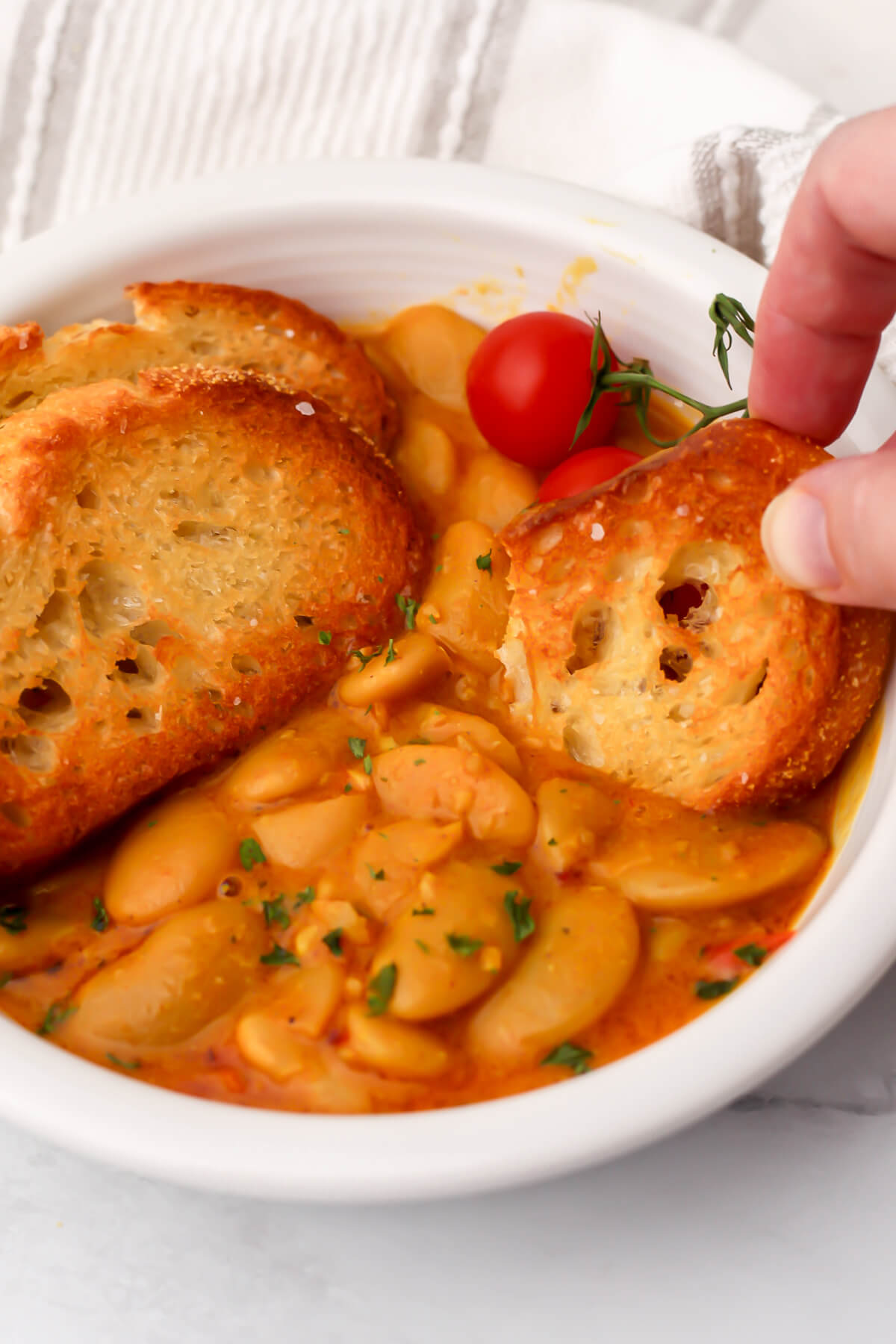 A white bowl filled with curried butter beans with crusty bread dipped into it.