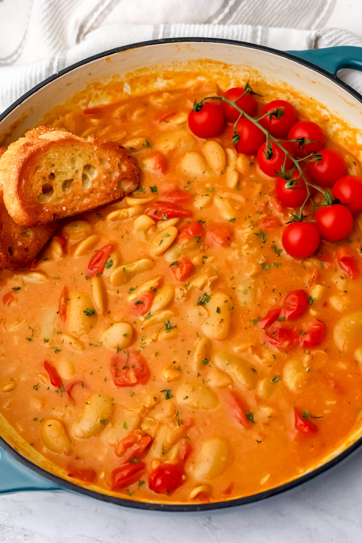 A top view of a blue skillet full of butter bean curry with sliced crispy bread on the side.