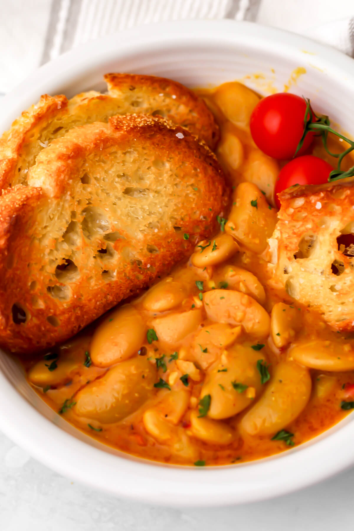 A white bowl filled with vegan butter bean curry with toasted bread on the side for dipping.