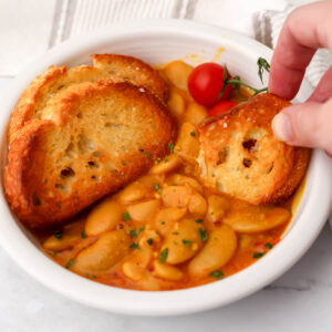 A bowl of curried butter bean with someone dipping bread into it.