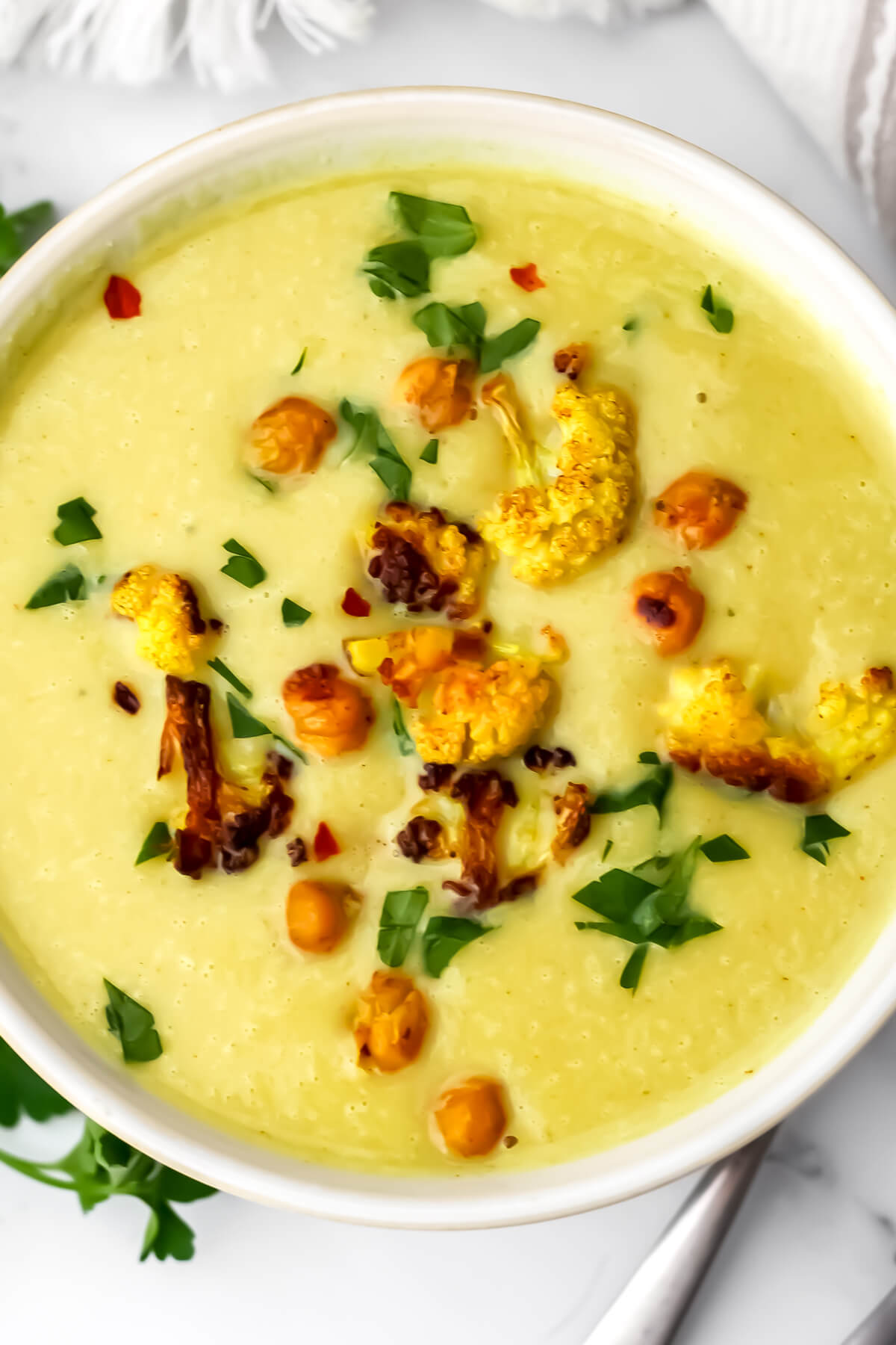 A top view of a creamy vegan curried cauliflower and chickpea soup garnished with roasted cauliflower.