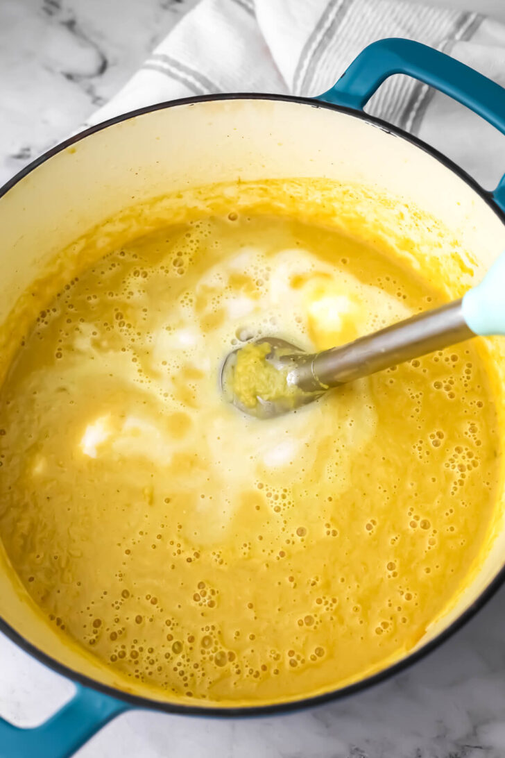 Pureeing curried cauliflower soup with coconut milk using an immersion blender.