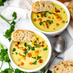 A top view of 2 white bowls filled with creamy curried cauliflower and chickpea soup and topped with roasted cauliflower and chickpeas.