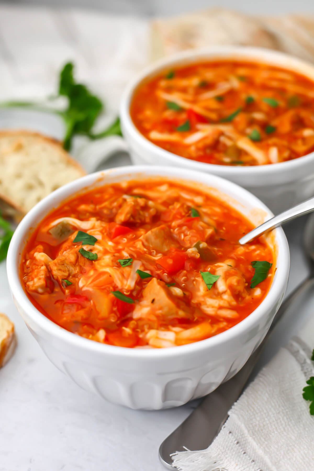 Two bowls of vegan stuffed pepper soup with bread on the side.