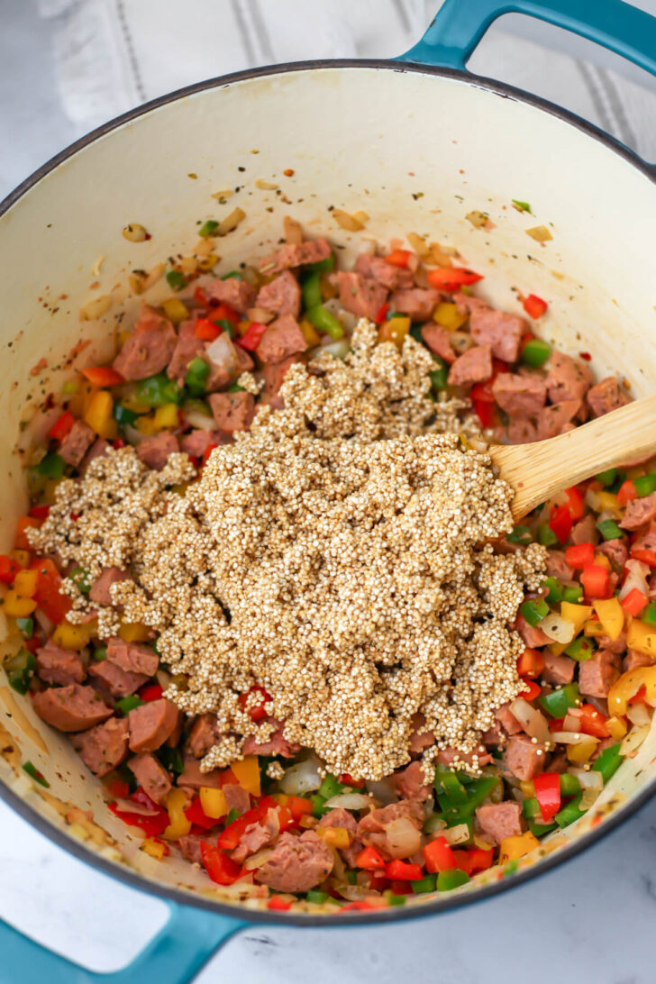 Quinoa added to sautéed veggies in a soup pot.