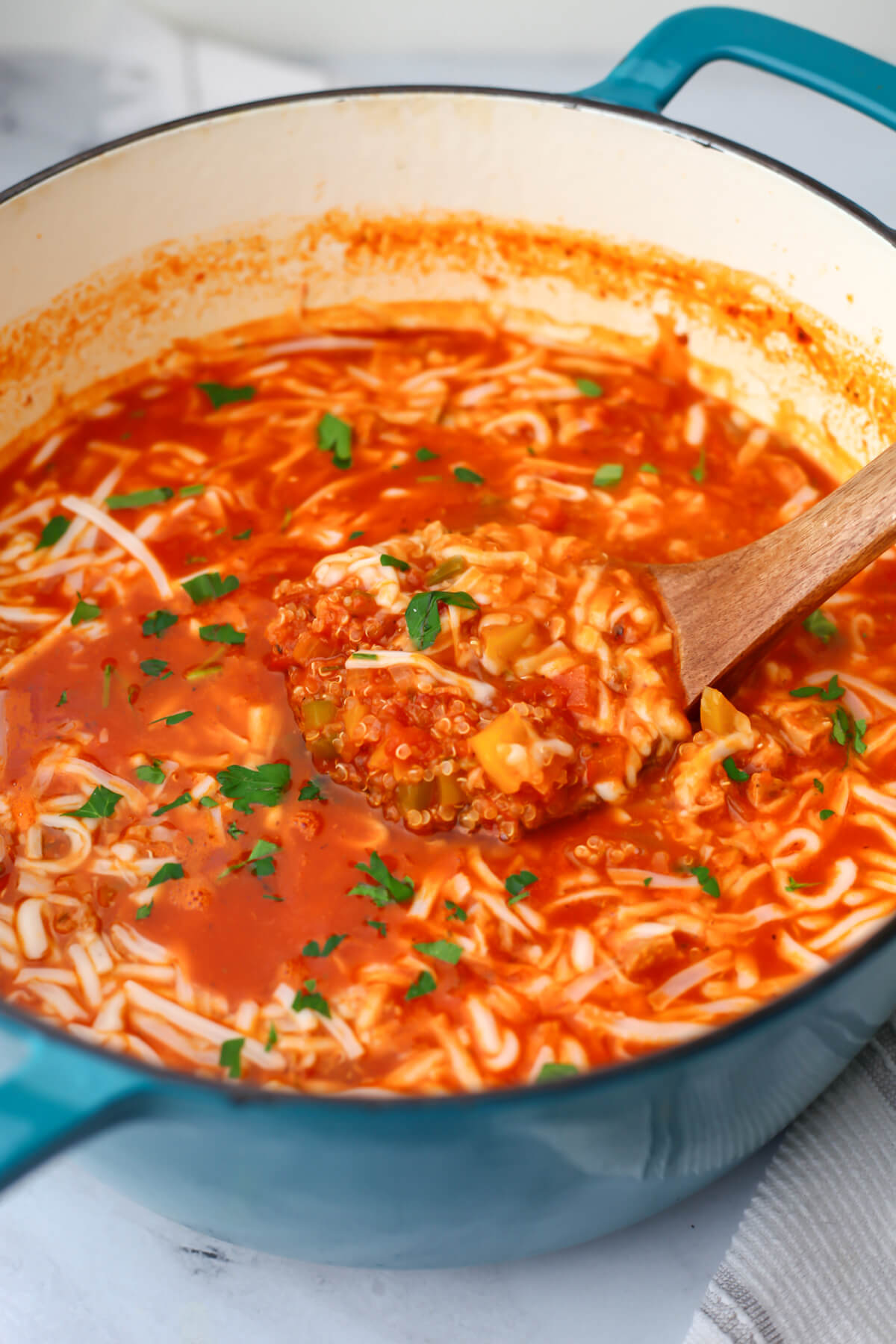 A large blue soup pot filled with vegan stuffed pepper soup being scooped out with a wooden ladle. 