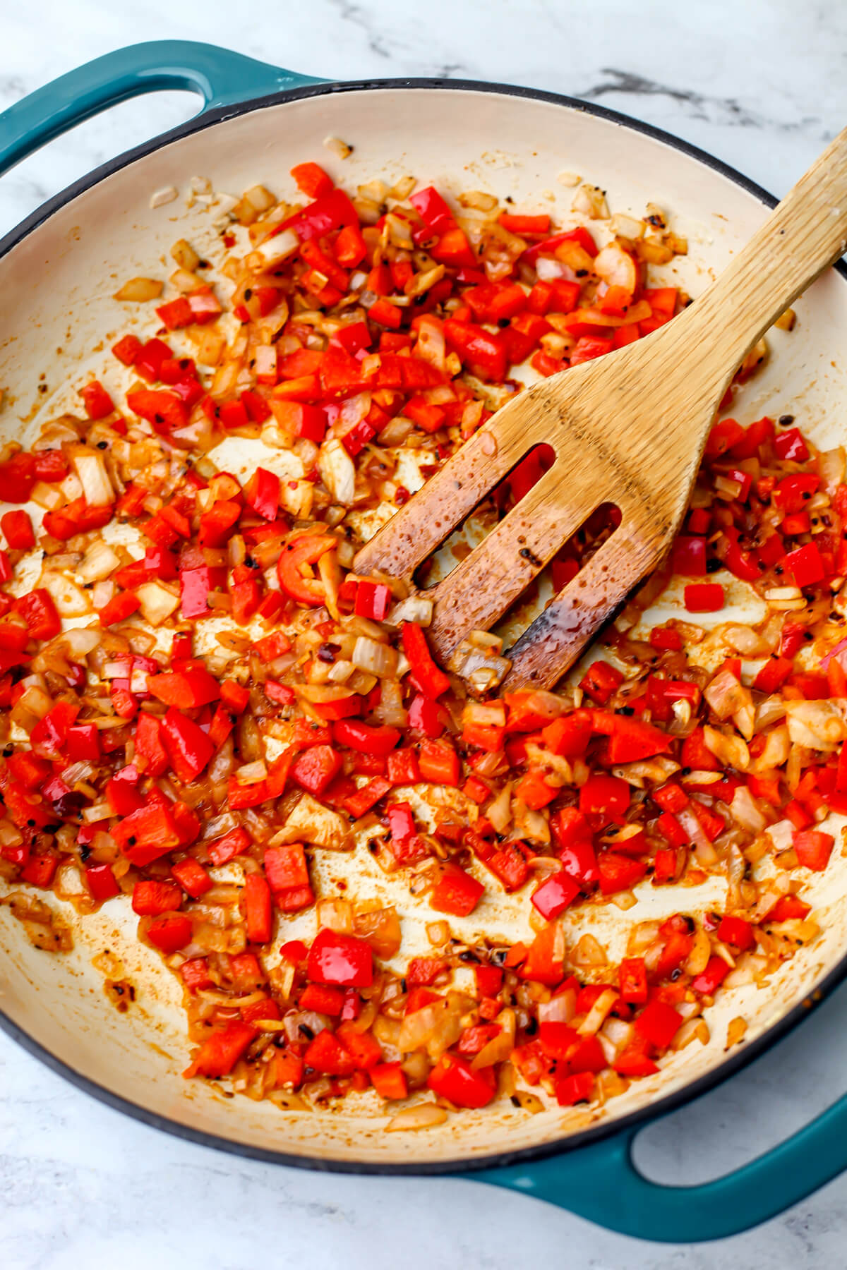 Onions and red bell peppers sautéing in a skillet.