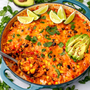 A skillet filled with vegan Mexican quinoa topped with cilantro, lime slices, and avacado.