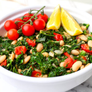 Kale and white bean salad with tomatoes served with lemon wedges.