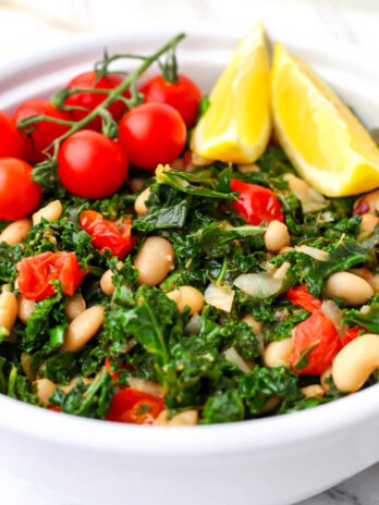 Kale and white bean salad with tomatoes served with lemon wedges.