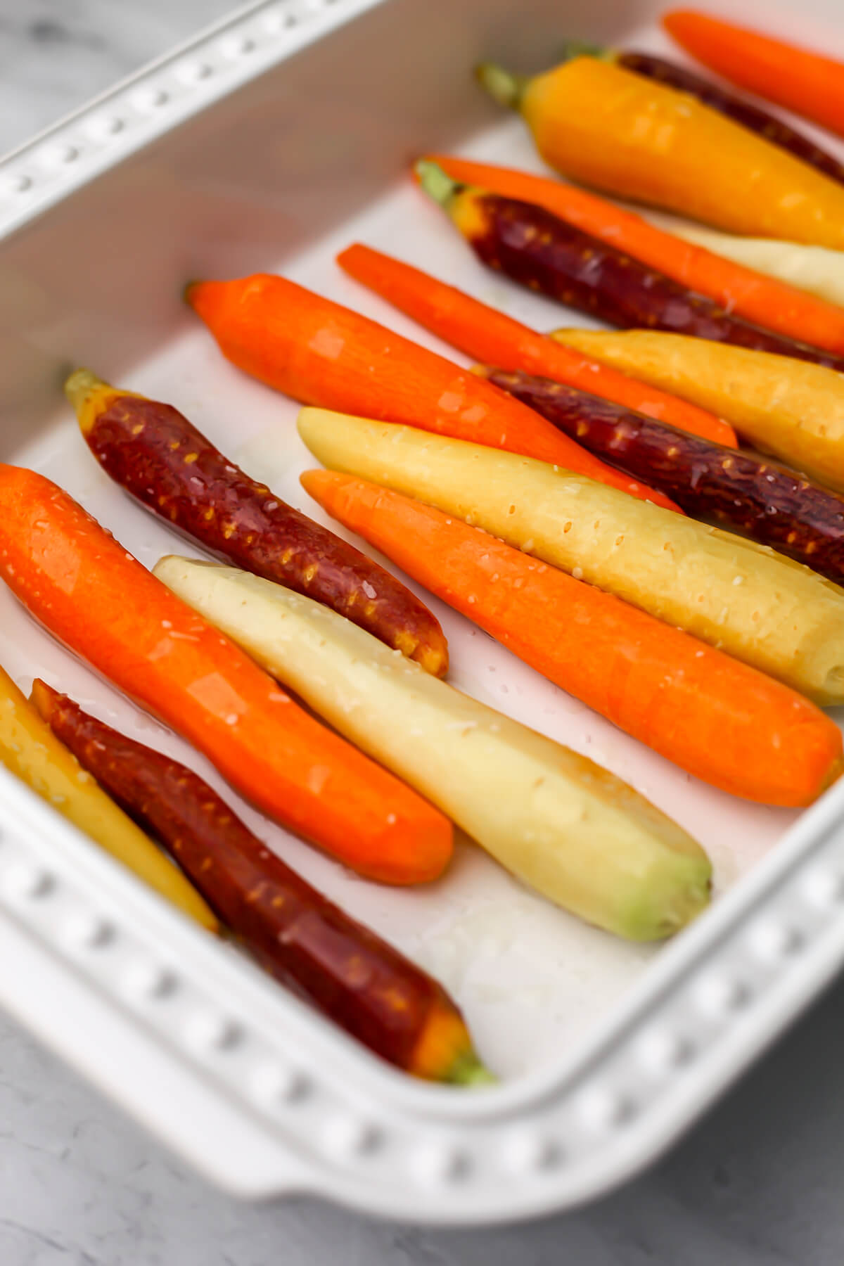 Rainbow carrots in a white baking dish before roasting.