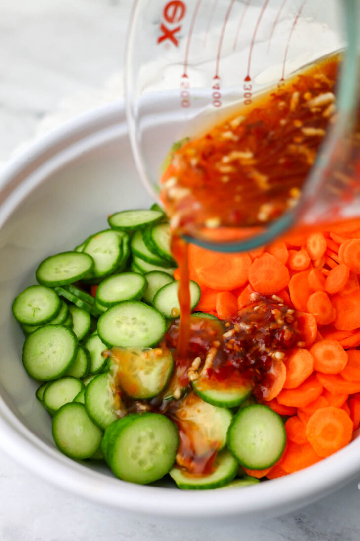 Pouring the dressing over the sliced carrots and cucumbers.