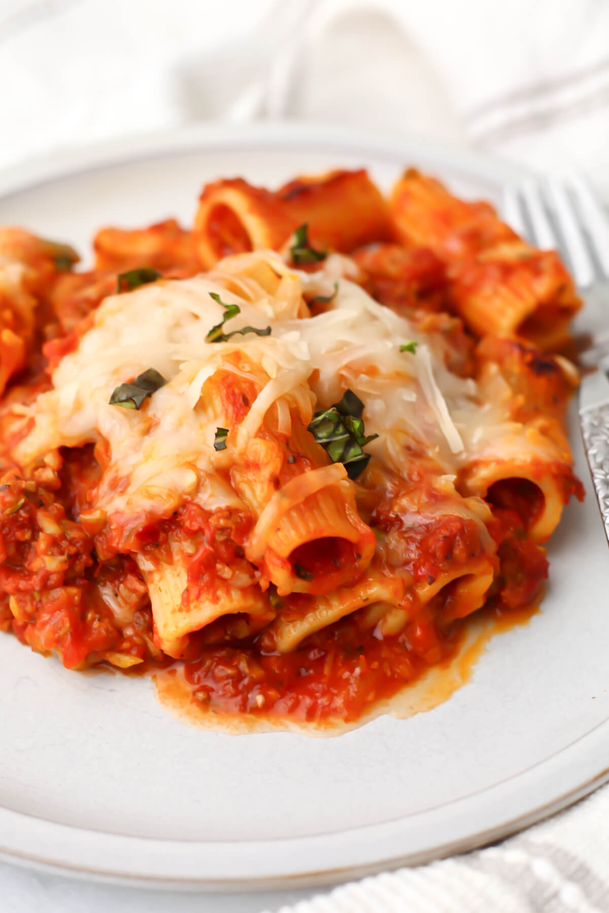 A white plate filled with vegan pasta bake made with rigatoni, Beyond crumbles, and hidden veggies.