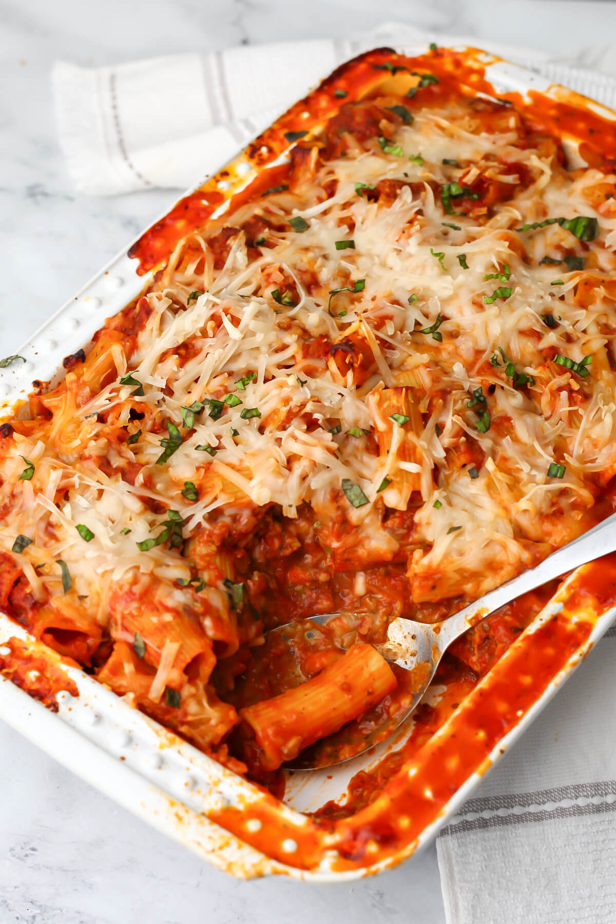 A top view of a casserole dish filled with vegan pasta bake with veggies, rigatoni noodles and vegan cheese melted on top.