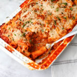 Vegan rigatoni pasta in a white baking dish with a scoop taken out of it.