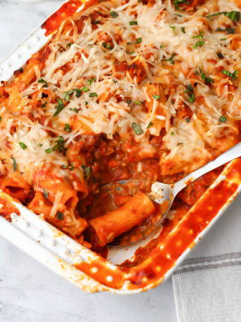 Vegan rigatoni pasta in a white baking dish with a scoop taken out of it.
