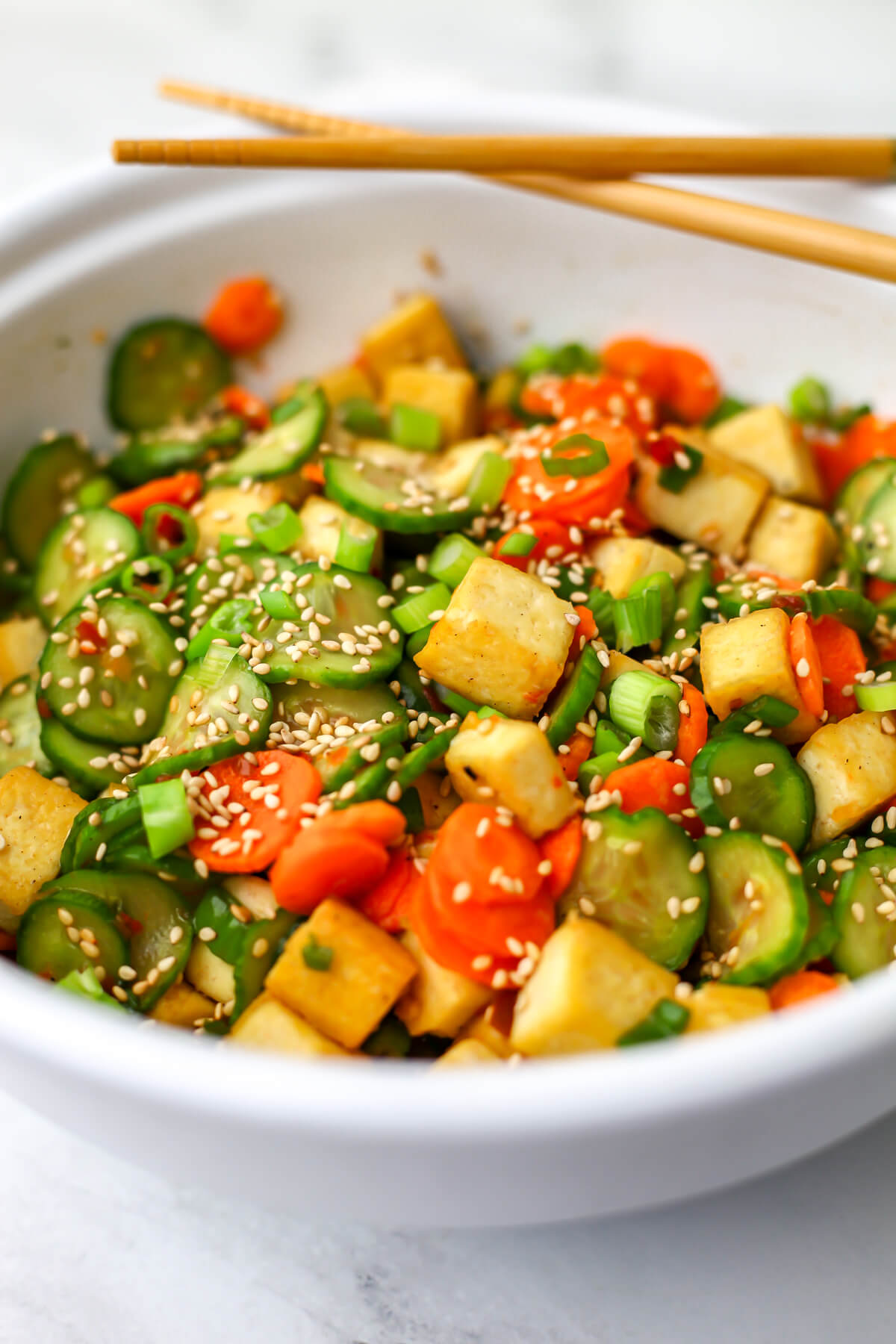 A white bowl filled with cucumber tofu salad with chop sticks balanced on the edge.