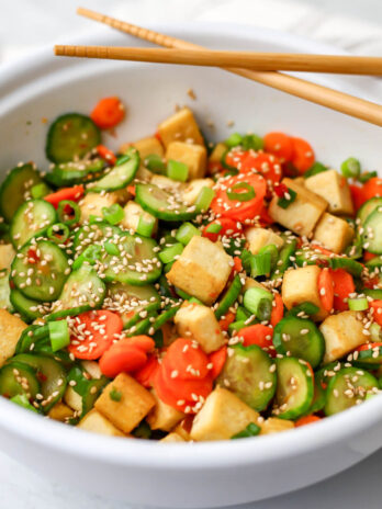 A white bowl filled with cucumber tofu salad with carrots, green onions, and sesame seeds.