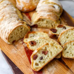 Vegan kalamata olive bread on a wooden cutting board cut into slices.