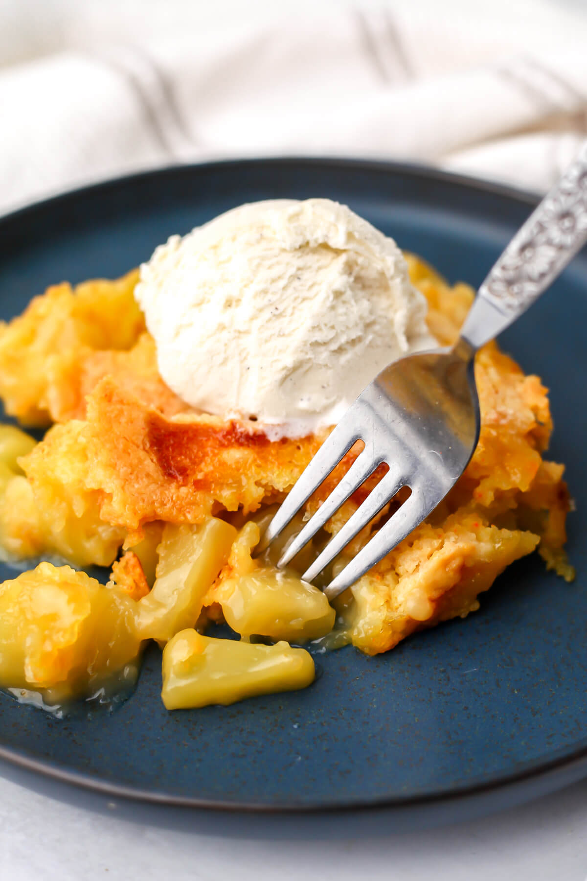 Vegan dump cake with pineapple with a scoop of ice cream on top with a fork in it.