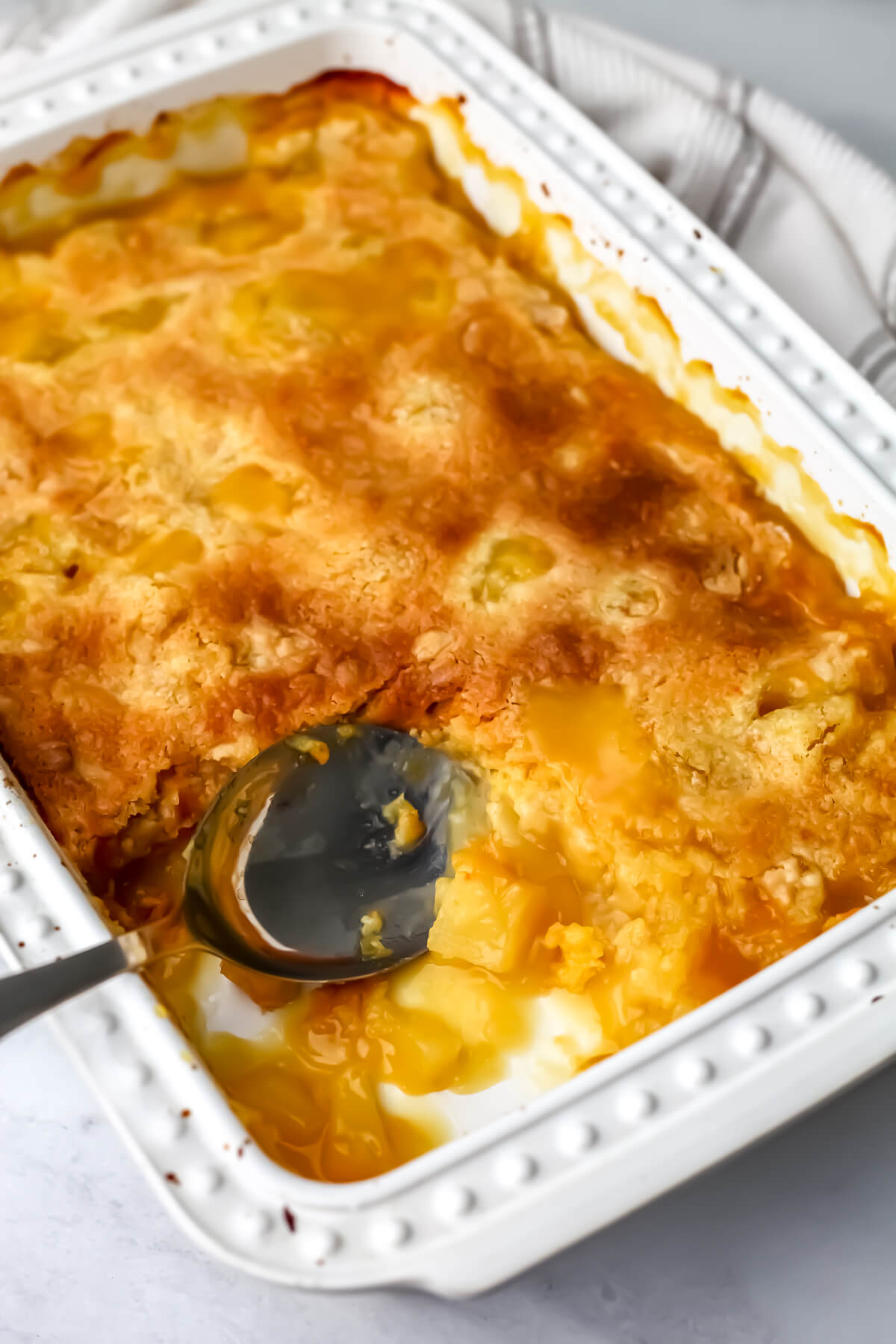 A vegan dump cake in a white baking dish being scooped up with a large spoon.