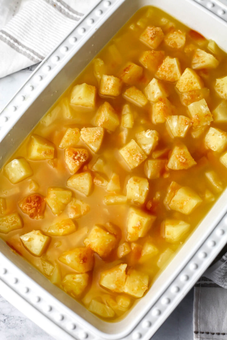 Canned pineapple and the liquid in a baking dish with brown sugar.