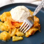 A vegan pineapple dump cake with vanilla ice cream on top and a fork picking up a piece of pineapple.